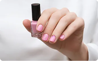 female hand with pink nail design holding nail polish bottle